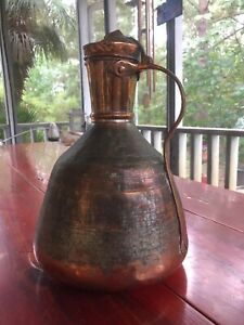 an old metal pitcher sitting on top of a wooden table next to a glass window