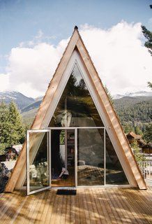 a house made out of wood and glass on top of a wooden deck with mountains in the background