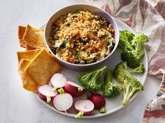 a white plate topped with broccoli, radishes and chips next to a bowl of dip