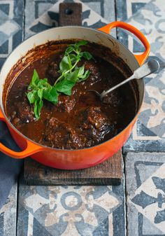 an orange pot filled with stew on top of a wooden cutting board