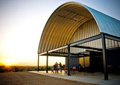 two people are standing in front of a large metal structure with the sun setting behind them