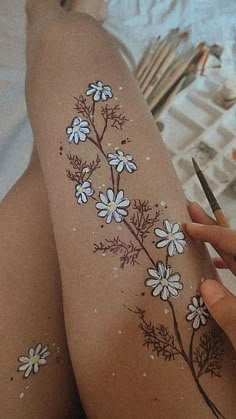 a woman with flowers painted on her legs holding a pair of scissors in front of her thigh