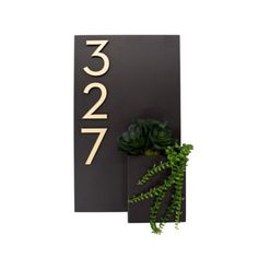 a house number sign next to a plant on a white background with the numbers twenty and seven