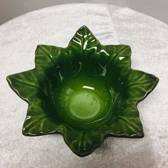 a green glass bowl sitting on top of a white cloth covered tableclothed surface