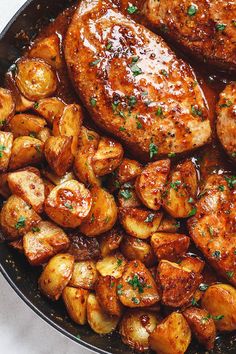 some meat and potatoes in a skillet on a white counter top with parsley