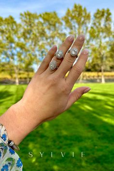 a woman's hand with two rings on it and some trees in the background