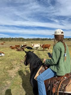 a woman riding on the back of a horse in a field full of cattle and cows