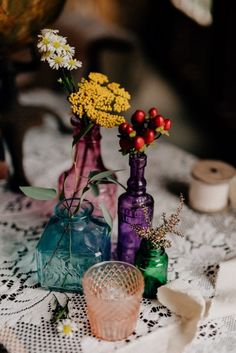 several vases with flowers in them sitting on a lace tablecloth next to thread spools