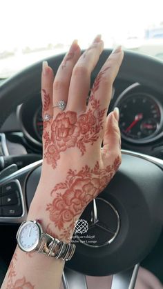 a woman's hand on the steering wheel of a car with henna tattoos