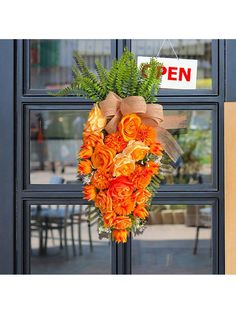 an orange and green wreath hanging on the front door of a building with a sign that says open