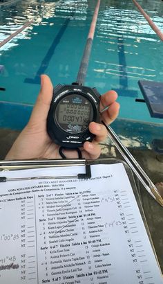 a person holding up a digital watch in front of a swimming pool with thermometer