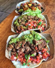 three burritos with meat, guacamole and salsa on them sitting on a wooden table