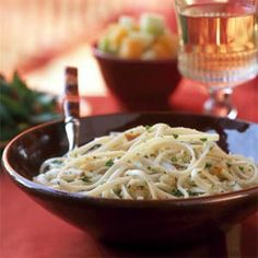 a bowl filled with pasta sitting on top of a table next to a glass of wine