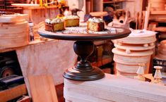 three cakes are on a cake stand in a room full of woodworking tools and other items