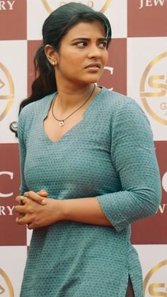 a woman standing in front of a wall with her hands folded and looking off to the side