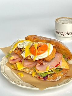 a sandwich with eggs, ham and cheese on it next to a cup of coffee