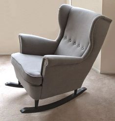 a grey rocking chair with buttons on the armrests is in front of a white wall