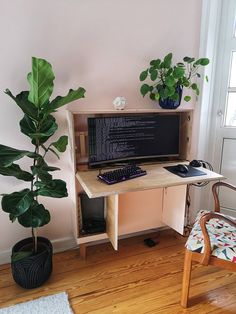 a desk with a computer on it next to a potted plant and a chair