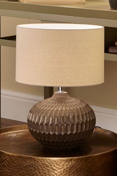 a table lamp sitting on top of a wooden table next to a mirror and book shelf