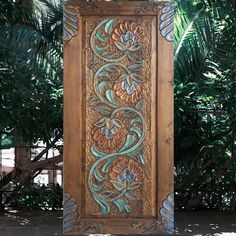 an intricately carved wooden panel with flowers and leaves on the outside, in front of palm trees