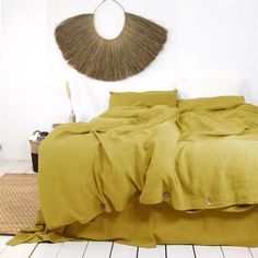 a bed with yellow sheets and pillows in a room next to a wicker wall decoration