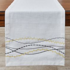 an embroidered table runner with yellow and black lines on white linen, sitting on a wooden table