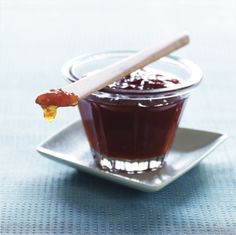 a small glass bowl filled with jelly on top of a silver plate next to a wooden spoon