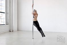 a woman is hanging upside down on a pole in an empty room with white walls