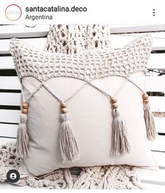 a white pillow with tassels on it sitting on a bench next to a blanket