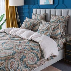 a bedroom with blue walls and a bed covered in paisley print sheets, pillow cases, and throw pillows