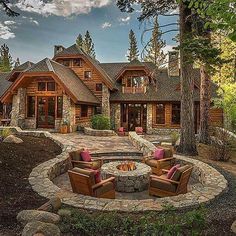 a large stone fire pit in front of a log cabin with two chairs around it