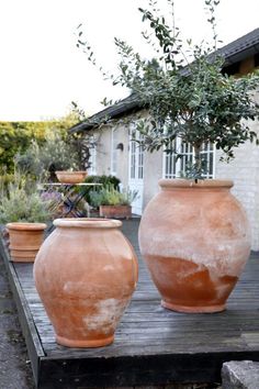 two large clay pots sitting on top of a wooden table next to a house and trees