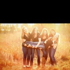 four beautiful young women posing for a photo in the grass with their arms around each other