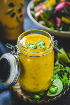 a glass jar filled with yellow liquid next to a bowl of green peppers and cilantro