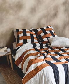 a bed with an orange, black and white comforter on it next to a night stand