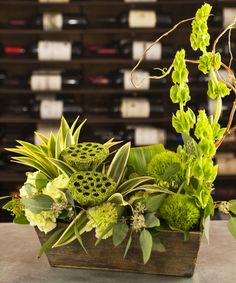 a wooden box filled with lots of green flowers and greenery next to wine bottles