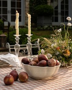 a bowl of fruit sitting on top of a table next to two candles and flowers