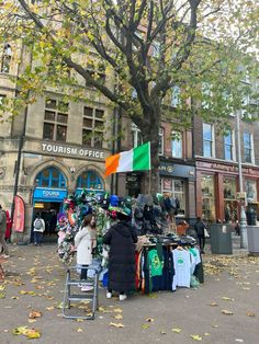 people are shopping at an outdoor market in front of a building with flags on it