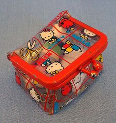 a hello kitty plastic box with scissors and other items in it on a blue surface