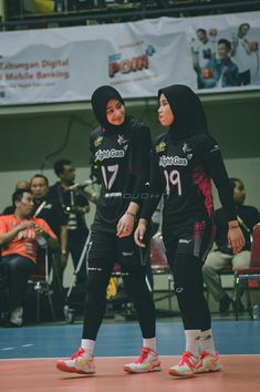 two women in black uniforms standing on a basketball court