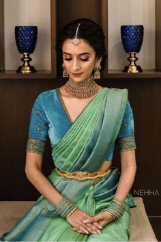 a woman in a green and blue sari sitting on a table with two vases behind her