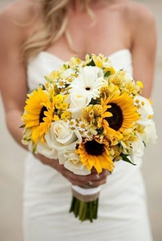 a bride holding a bouquet of sunflowers and other flowers on her wedding day