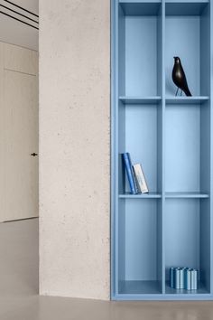 a blue shelf with books and a black bird on it in an empty room next to a door