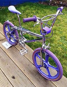 a purple and white bicycle parked on top of a wooden deck next to a green field