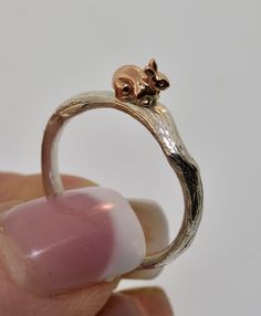 a hand holding a tiny silver ring with a cat on it's back end