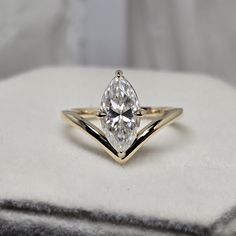 a yellow gold ring with a pear shaped diamond in the center on a white cushion