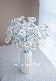 a white vase filled with blue and white flowers on top of a table next to a window