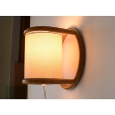 a wall light with a white fabric shade on it's arm and a wooden frame around the lamp