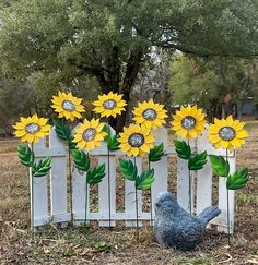 sunflowers are placed in front of a picket fence with a bird figurine