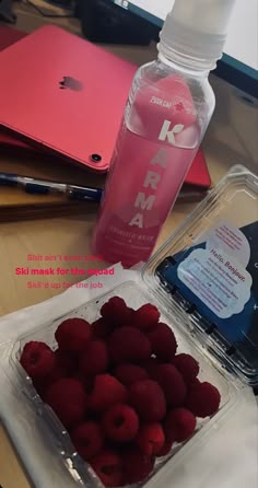 raspberries in a plastic container next to a water bottle and notebooks on a desk